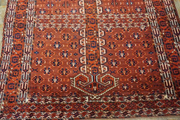 Low-pile red rug with dense geometric patterns in blue, orange, and cream on light-colored flooring.