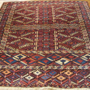 Red, blue, and cream traditional geometric rug with a thick pile rests on wooden planks.