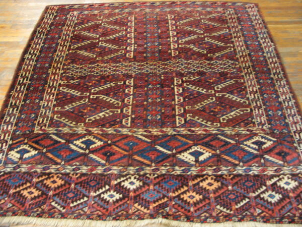 Red, blue, and cream traditional geometric rug with a thick pile rests on wooden planks.