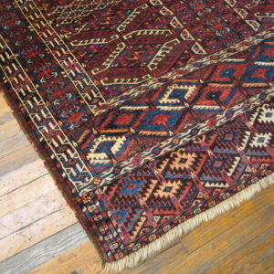 Red, blue, and tan geometric rug with fringe lying diagonally on distressed wood plank flooring.