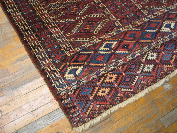 Red, blue, and tan geometric rug with fringe lying diagonally on distressed wood plank flooring.