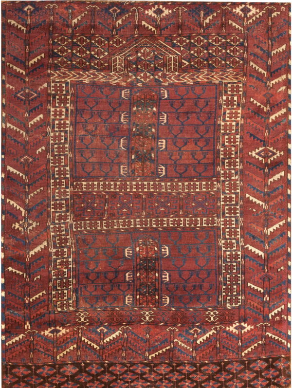 Deep red rug with complex geometric designs, dark blue motifs, and a vertically segmented field.