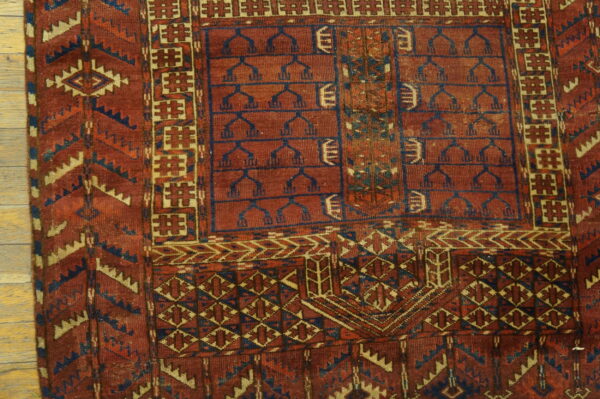 Red, navy, and beige geometric patterned rug featuring traditional tree motifs and complex borders on a wood floor.