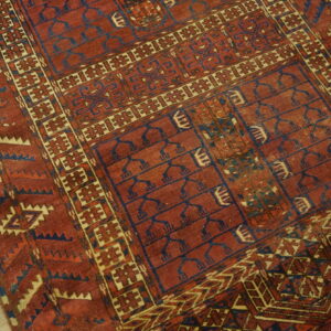 Low-pile red rug with blue and tan geometric tribal motifs rests on light wooden flooring.