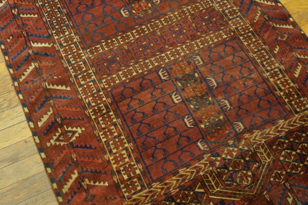 Low-pile red rug with blue and tan geometric tribal motifs rests on light wooden flooring.