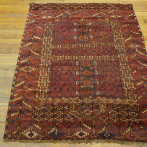 A deep red geometric rug featuring blue and tan borders rests on light-colored hardwood floorboards.