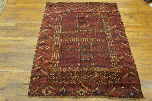 A deep red geometric rug featuring blue and tan borders rests on light-colored hardwood floorboards.