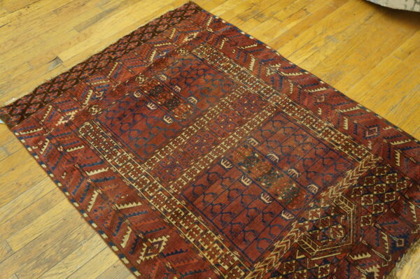 A deep red rug featuring complex geometric patterns in dark blue and cream lies on a wood plank floor.