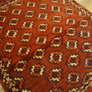 Rust-colored rug featuring repeating geometric medallions in cream, orange, and navy on hardwood flooring.