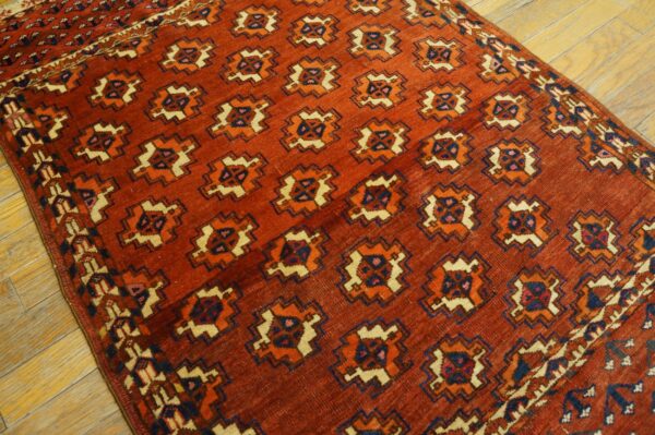 Rust-colored rug featuring repeating geometric medallions in cream, orange, and navy on hardwood flooring.