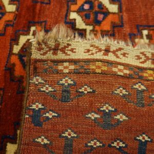 Close-up of a terracotta rug folded, revealing geometric pile patterns and a tight, patterned flatwoven reverse.