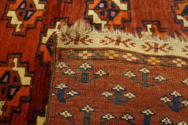 Close-up of a terracotta rug folded, revealing geometric pile patterns and a tight, patterned flatwoven reverse.