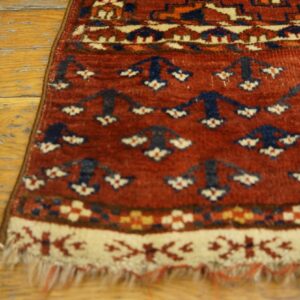 A rust colored rug with navy and cream geometric patterns is shown on distressed hardwood flooring.