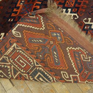 Geometric brown, red, and blue rug folded back, exposing its kilim end and fringe on a wood floor.