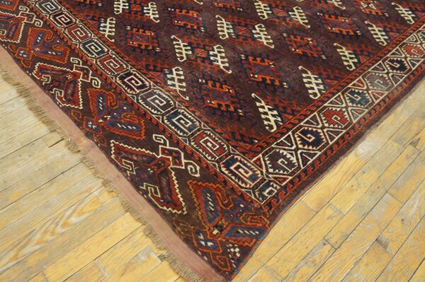 Dark geometric rug featuring red, blue, and cream motifs rests on light, distressed wood plank flooring.