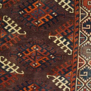 Dark maroon rug close-up showing geometric motifs in cream, dark blue, and rust, bordered by wood flooring.