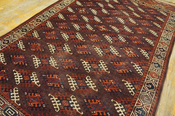 Maroon geometric rug featuring repeating patterns in rust, navy, and cream displayed on light wood plank flooring.