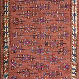Dusty red rug with repeating blue, purple, and rust geometric symbols framed by a multi-layered border.