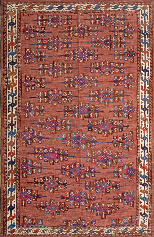 Dusty red rug with repeating blue, purple, and rust geometric symbols framed by a multi-layered border.