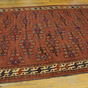 Geometric patterned low-pile rug in rust, navy, and cream colors on a worn hardwood floor.
