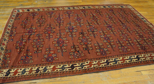 Geometric patterned low-pile rug in rust, navy, and cream colors on a worn hardwood floor.