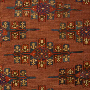 Detailed view of a red rug with repeating blue, red, and tan geometric motifs and a complex patterned border.