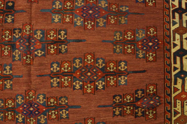 Detailed view of a red rug with repeating blue, red, and tan geometric motifs and a complex patterned border.