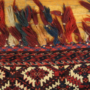 Multicolored tassels and a red and navy geometric rug border rest upon wooden flooring.