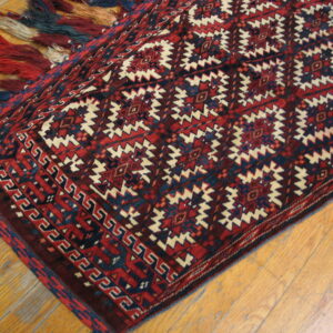 Red and navy geometric rug with cream accents and thick multicolored fringe on wooden flooring.