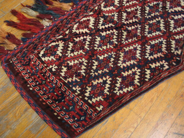 Red and navy geometric rug with cream accents and thick multicolored fringe on wooden flooring.