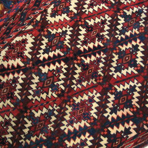 Geometric rug pattern in red, navy, and cream, featuring thick fringe and visible wooden floor.