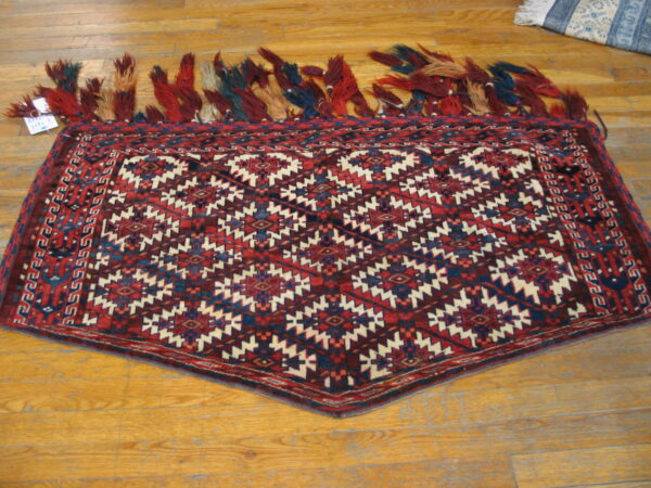 Tapered red and navy tribal rug with heavy multicolored fringe lies on wooden flooring.