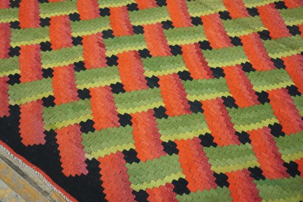 Geometric flatweave rug with interlocking zig-zag blocks in bright green, red-orange, and black colors.