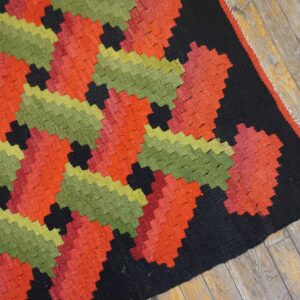 Flatweave rug featuring repeating stepped geometric patterns in vibrant red, green, and black on wood floor.