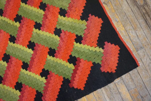 Flatweave rug featuring repeating stepped geometric patterns in vibrant red, green, and black on wood floor.