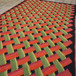 Red, green, and black flatweave rug displaying a diagonal zigzag pattern over light wood flooring.