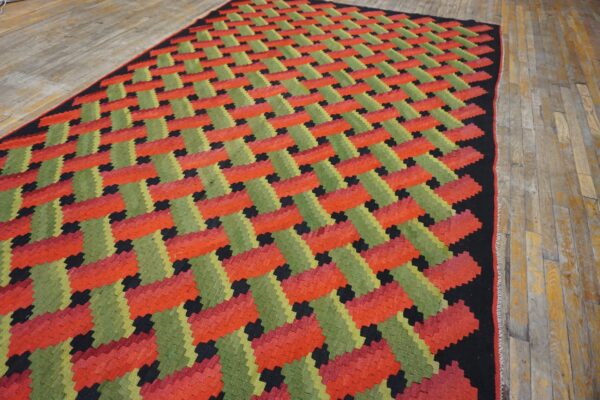 Red, green, and black flatweave rug displaying a diagonal zigzag pattern over light wood flooring.