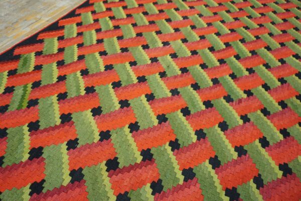 Low-profile rug featuring interlocking geometric patterns in bright red, olive green, and black on wood flooring.