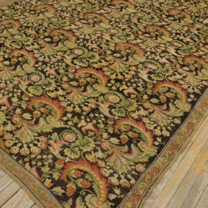 A large dark rug with dense green, tan, and red floral motifs on light wood flooring.