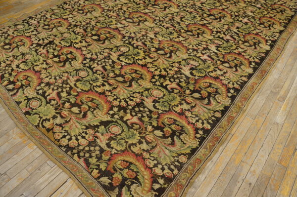 A large dark rug with dense green, tan, and red floral motifs on light wood flooring.