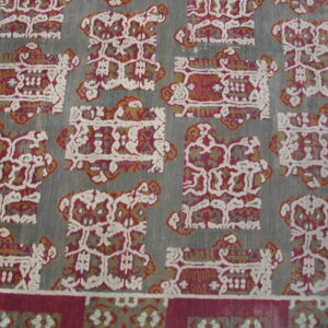 The rug has a slate grey ground and repeating rectangular motifs in burgundy, cream, and mustard yellow.