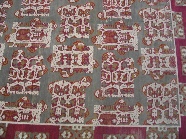 The rug has a slate grey ground and repeating rectangular motifs in burgundy, cream, and mustard yellow.