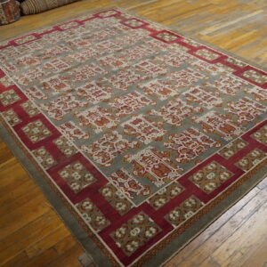 A large rug with red and gray geometric patterns rests on wide plank wooden flooring.