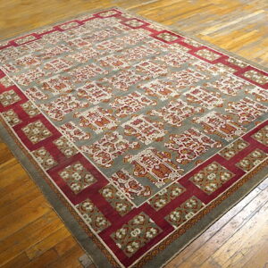 Low pile rug with a gray field and repeating red, rust, and ivory motifs on distressed wood planks.