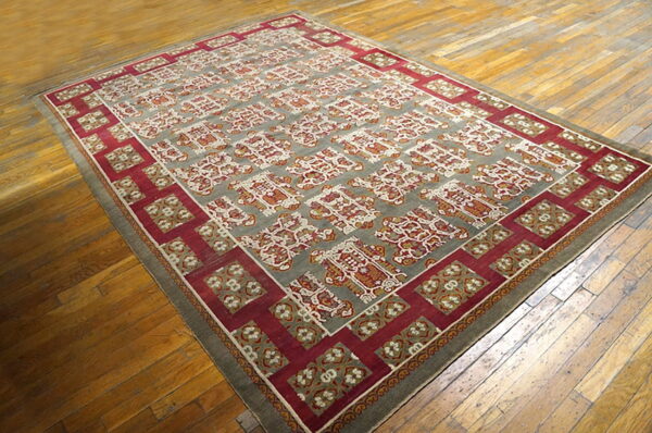 Low pile rug with a gray field and repeating red, rust, and ivory motifs on distressed wood planks.