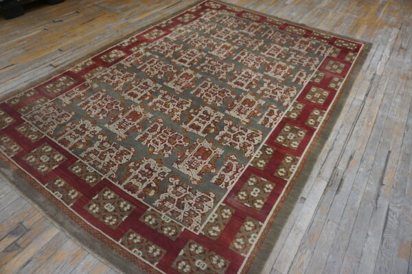 Muted gray and red rug with stylized pattern lies on distressed, wide-plank wood flooring.
