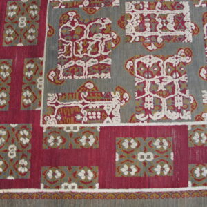 Gray, magenta, and gold rug featuring geometric motifs and textured white outlines near wood flooring.