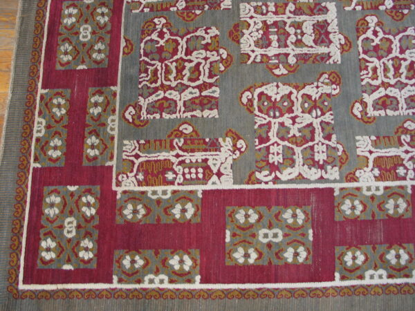 Gray, magenta, and gold rug featuring geometric motifs and textured white outlines near wood flooring.