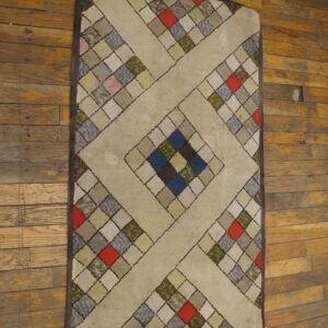 Beige rug with a colorful geometric square patchwork design, including red and blue, on distressed wood planks.