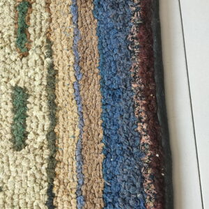 High-pile looped rug showing abstract stripes in tan, blue, burgundy, and cream against white tiled flooring.